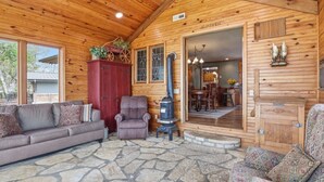 Interior acolhedor de uma cabana, com piso de pedra, um sofá, uma poltrona, um armário vermelho e fachada revestida de madeira.