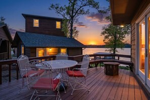 A wooden deck with a round table and chairs, overlooking a body of water at sunset. - Historic Harbor - Timeless, Location & 2 Slips! (Lake Ozark)
