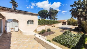 Ein Haus mit Terrasse, Steinboden und einem Garten mit verschiedenen Pflanzen.