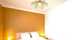 Habitació d'hotel amb paret de panells de fusta, llit amb roba de llit blanca, dues làmpades laterals i una lluminària de sostre singular.