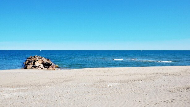 Una platja amb un promontori rocos i mar tranquil·la.