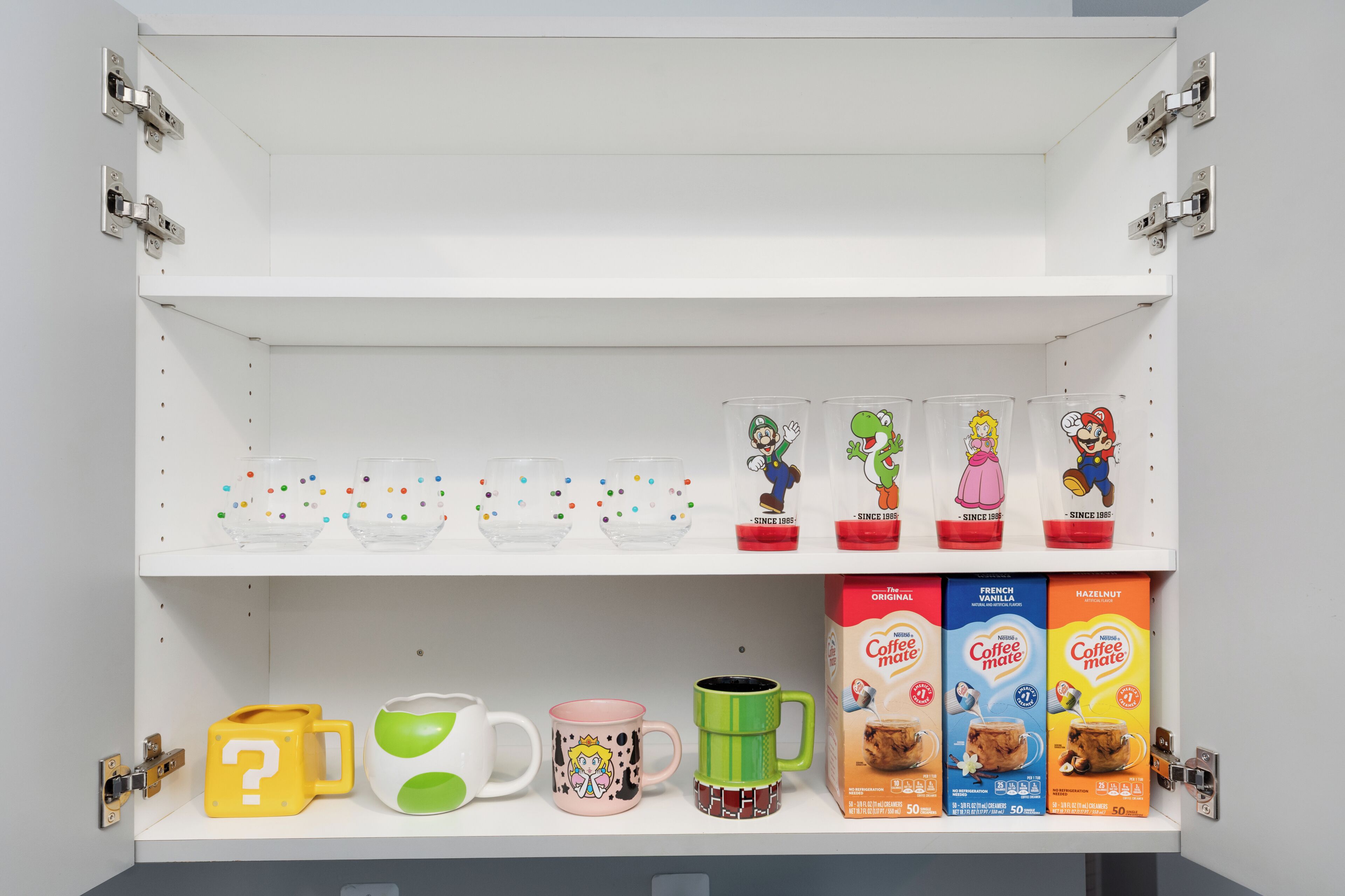 Un estante con varias tazas de café, una taza verde y cajas de Coffee Mate.