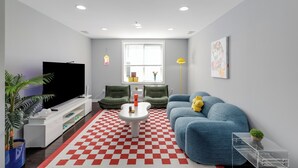 Een woonkamer met een televisie, bank, stoelen, salontafel en een zwart-wit geruit vloerkleed.