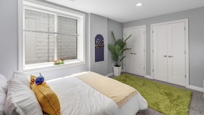 Een slaapkamer met een bed, een raam, een groen vloerkleed en een witte deur.