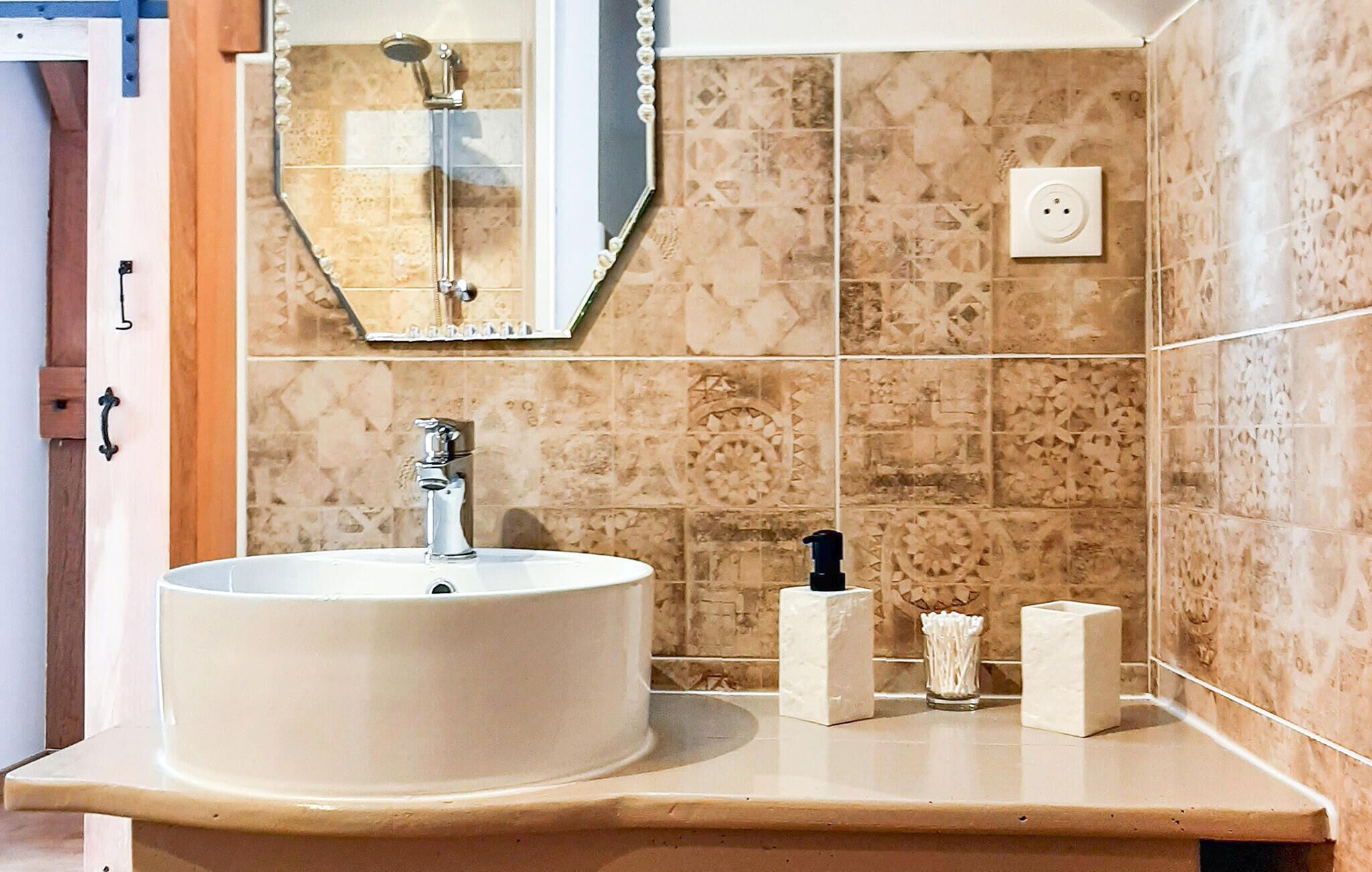 Un baño con un lavabo redondo, un espejo y baldosas estampadas.