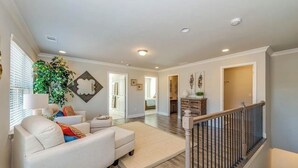 A spacious living room with a sofa, a coffee table, and a large plant. There is a staircase with a wooden railing leading to an upper level. - Luxury Gated Townhome For Full World Cup Stay w/2 Car Garage + Safe & Private (Atlanta)