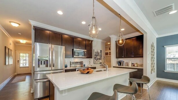 A modern kitchen with stainless steel appliances, a large island with bar stools, and pendant lighting. - Luxury Gated Townhome For Full World Cup Stay w/2 Car Garage + Safe & Private (Atlanta)