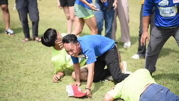 A group of people on a grassy field, some in athletic wear, with one person lying on the ground.