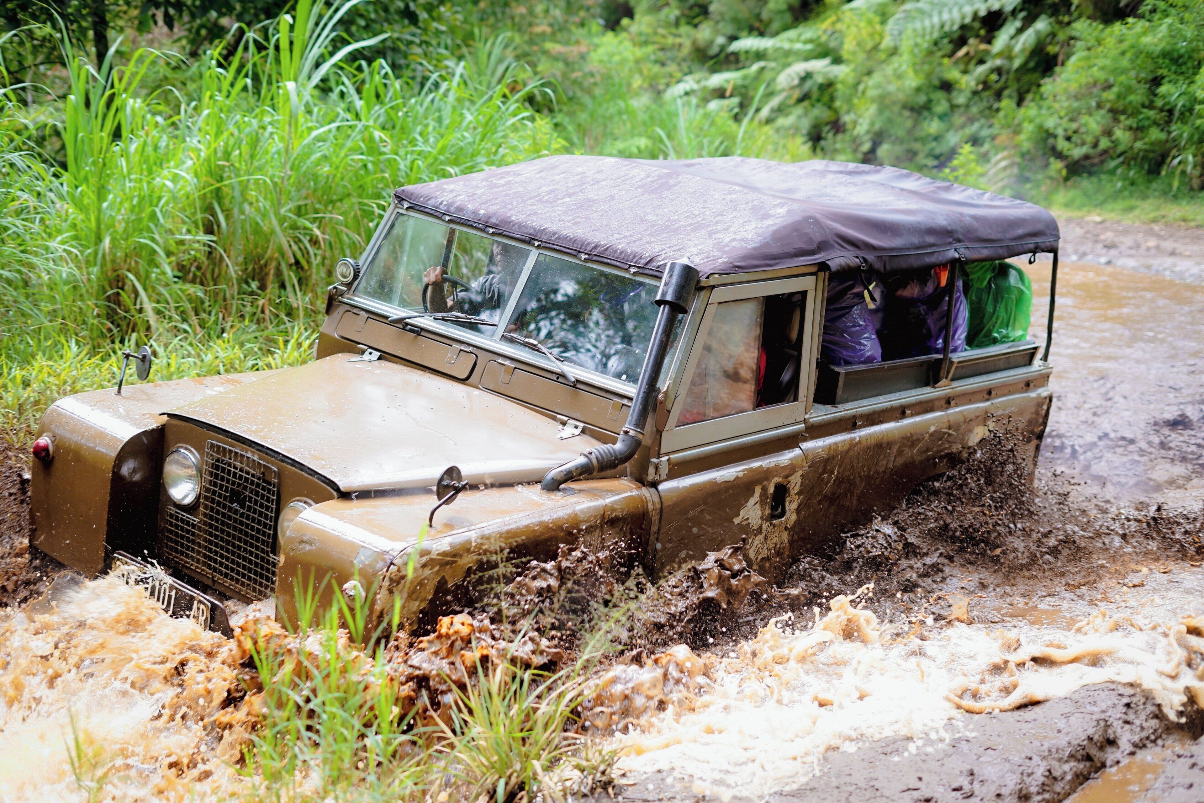 A vehicle navigating through a muddy terrain with passengers visible inside.