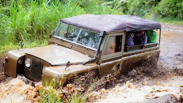 A vehicle navigating through a muddy terrain with passengers visible inside.