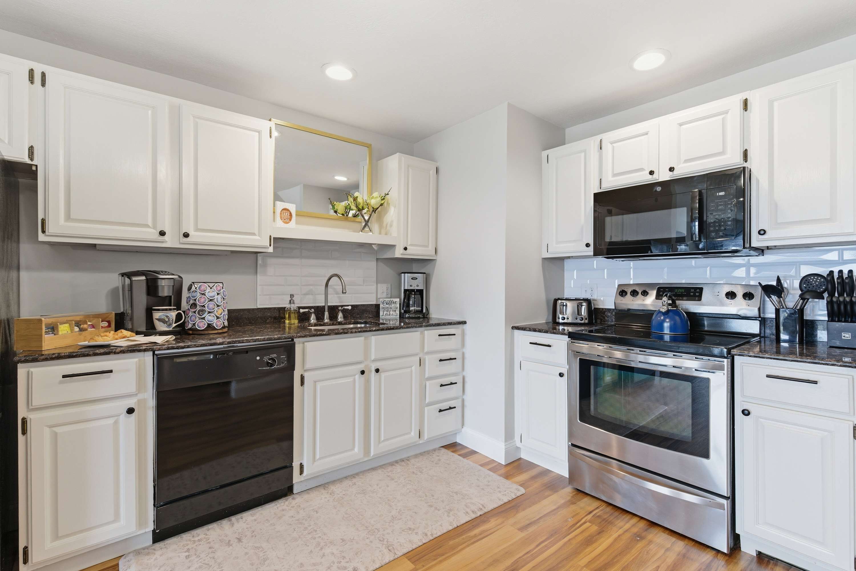 A modern kitchen with white cabinets, stainless steel appliances, and a wooden floor.