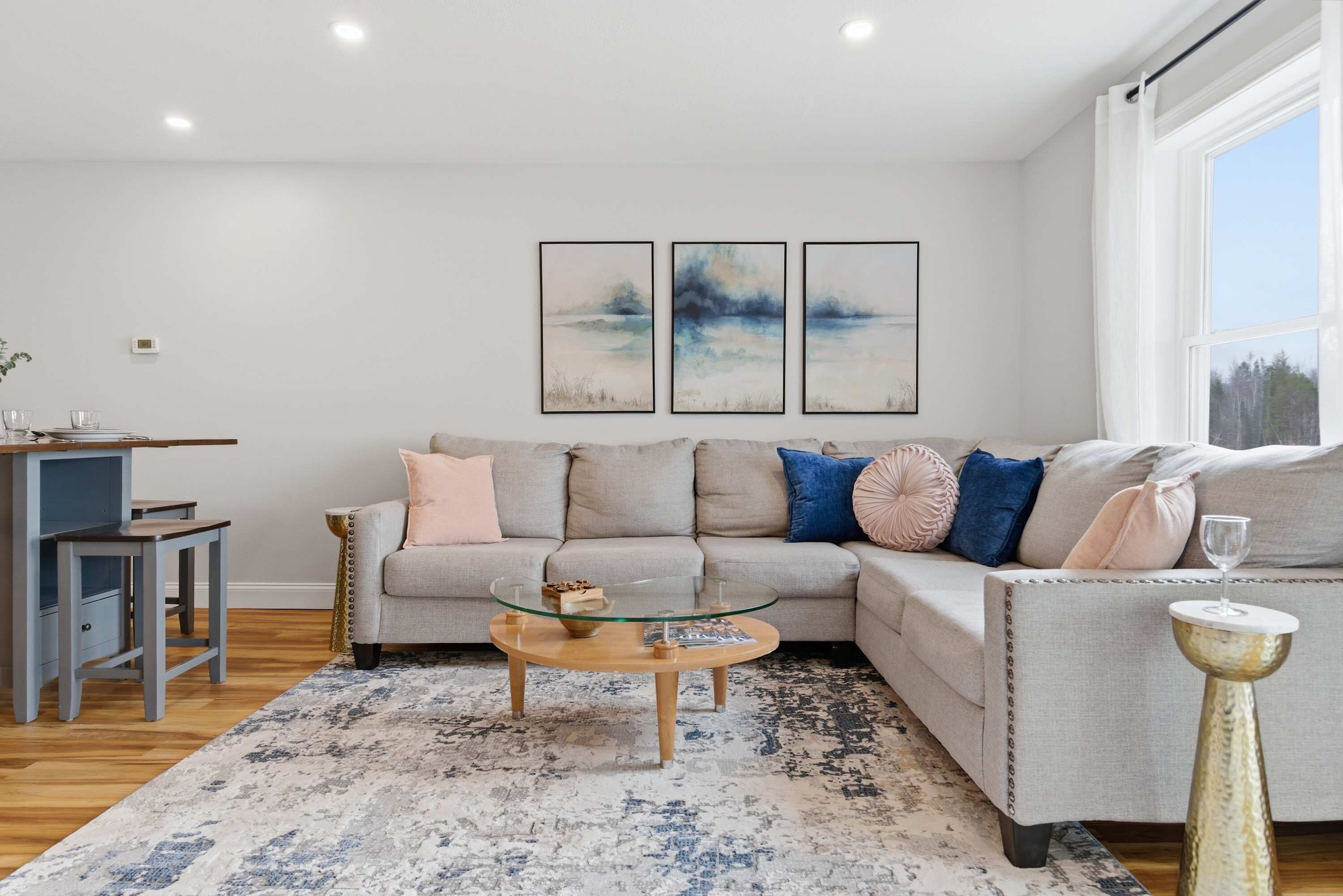 A living room with a sectional sofa, a glass coffee table, a patterned rug, and artwork on the wall.
