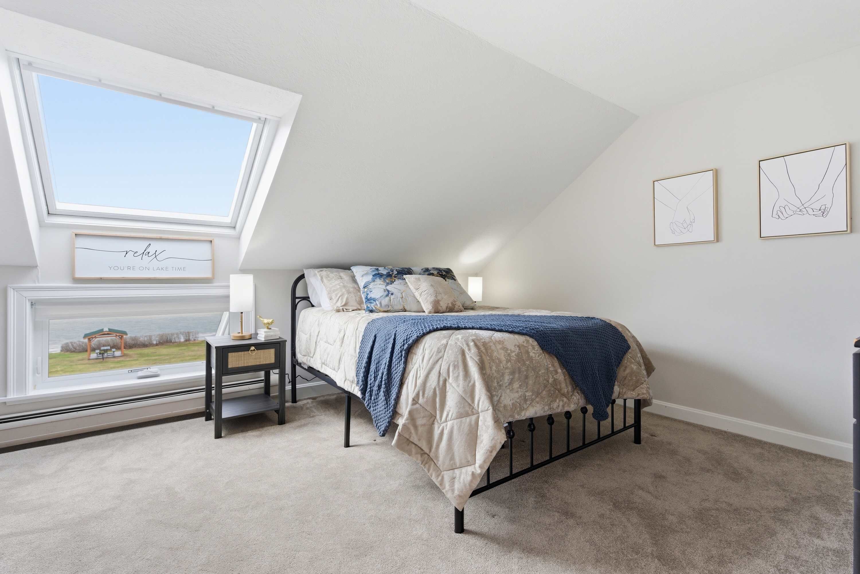 A bedroom with a bed, a nightstand, a window, and two wall art pieces.