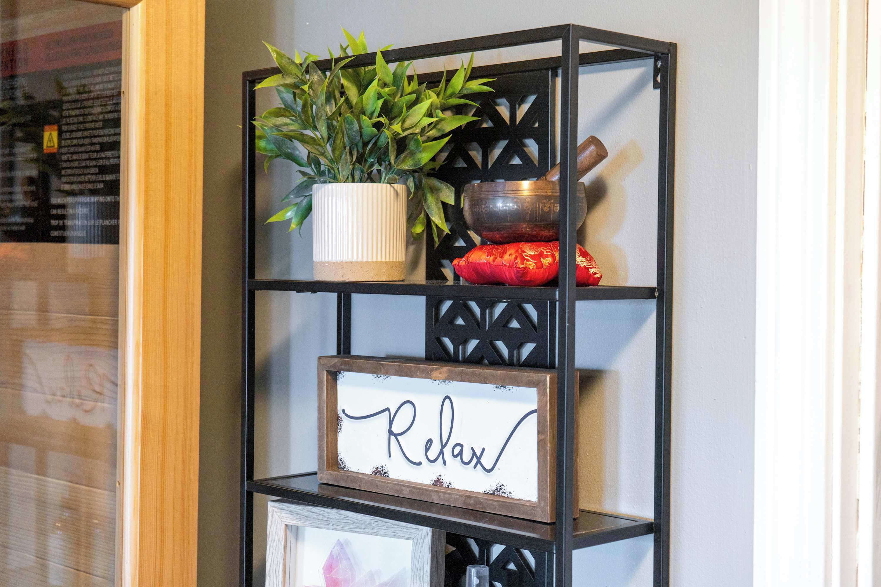 A black metal shelf with a potted plant, a bowl, and a framed sign with the word 'Relax'.
