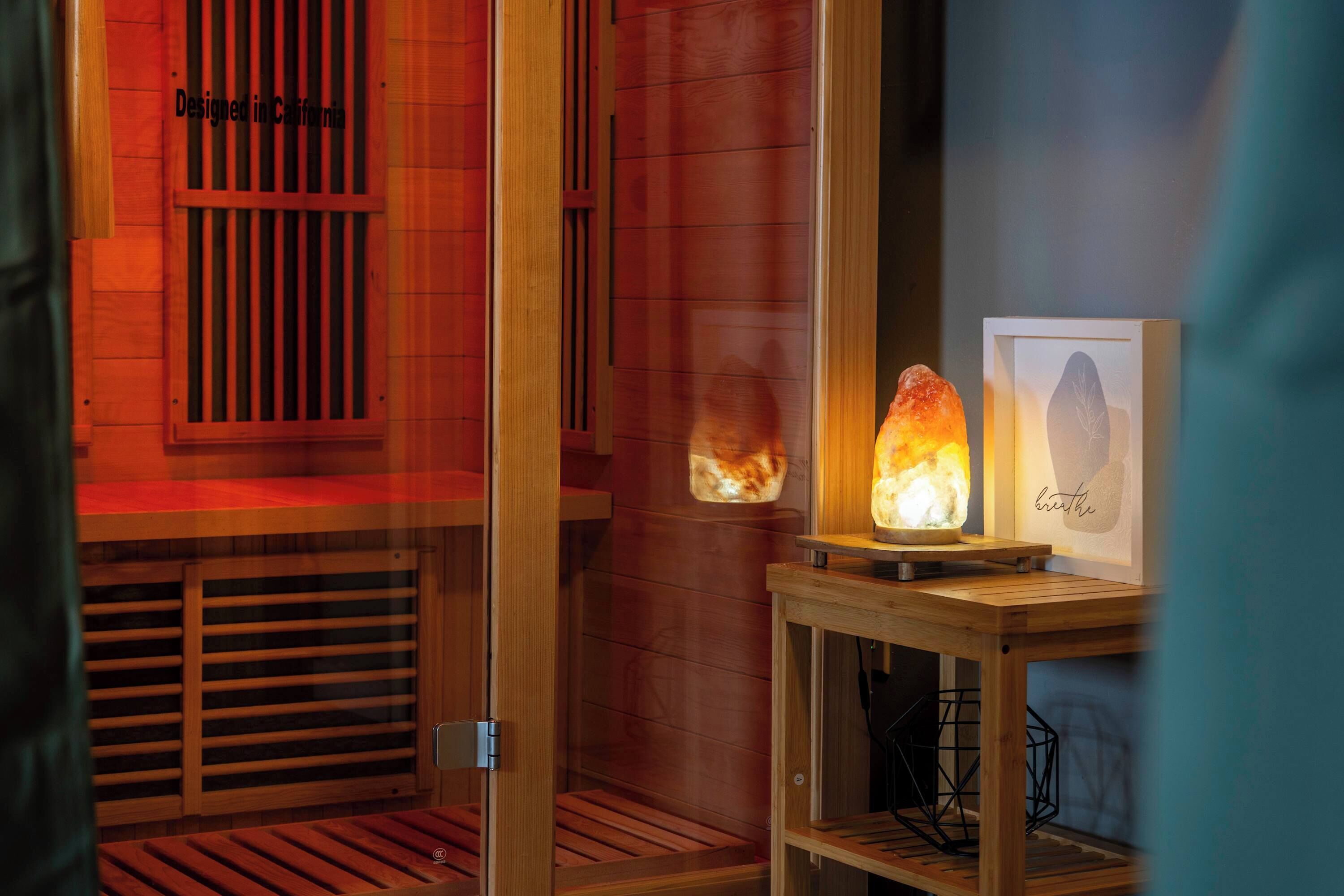 A sauna room with wooden benches, a glass door, and a framed artwork on a shelf.