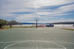 Un terrain de basket en plein air avec un panier, un camion bleu et un lac en arrière-plan.