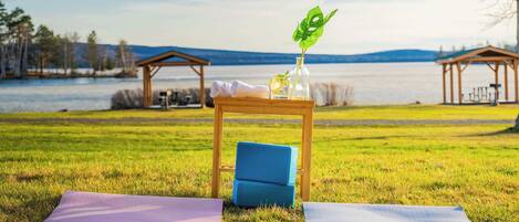 A grassy area with a wooden table, a blue chair, and a yoga mat.