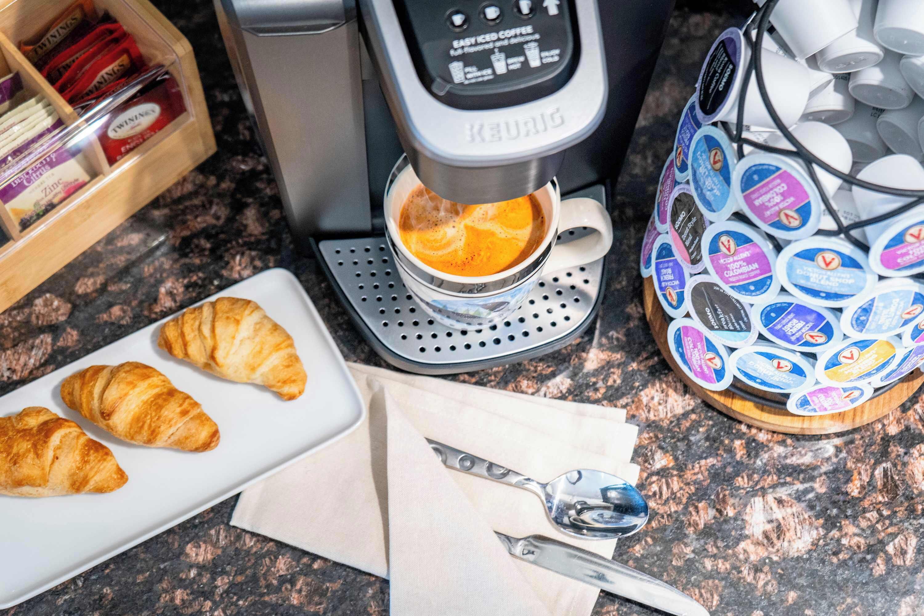 A coffee machine, croissants, and a tray of coffee pods on a kitchen counter.