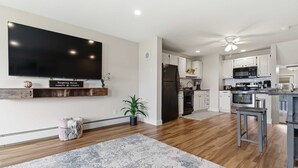 Eine moderne Küche mit Flachbildfernseher, Holzschränken, einem Kühlschrank und einem Essbereich mit Hockstühlen.