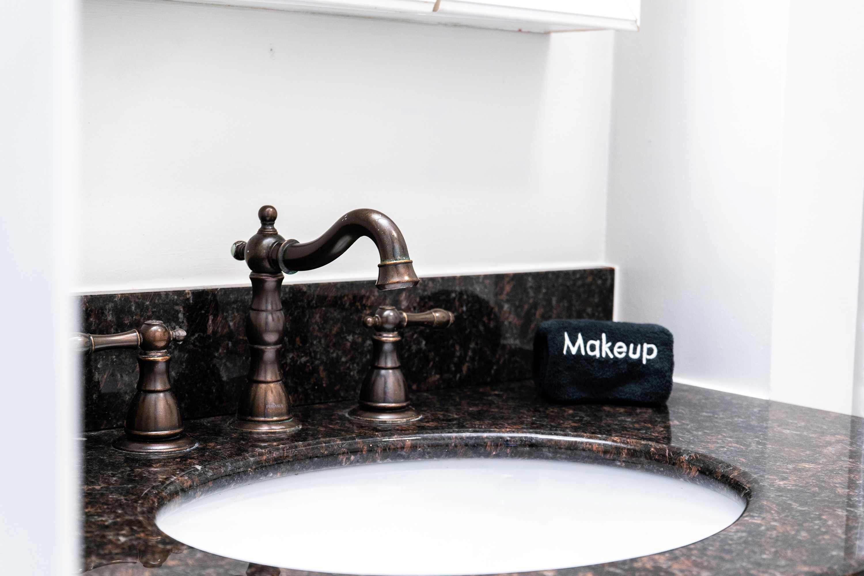 Een badkamer met een marmeren wastafel, een kraan in vintage stijl en een make-up tas op het aanrecht.