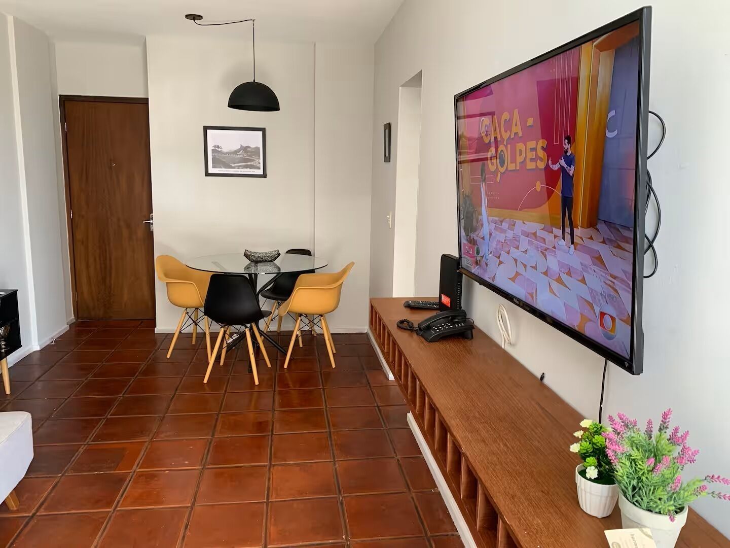 Ein Essbereich mit einem runden Tisch, vier Stühlen, einem Fernseher an der Wand und einer Holzbank.