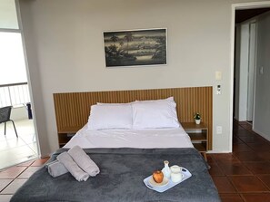 A hotel room with a bed, a painting, a tray with an apple and cups, and a balcony. - Oceanfront apartment in Barra da Tijuca (Rio de Janeiro)