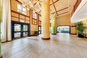 Eine geräumige Lobby mit großen Säulen, einem Empfangstresen und einer Treppe, die in einen oberen Bereich führt.