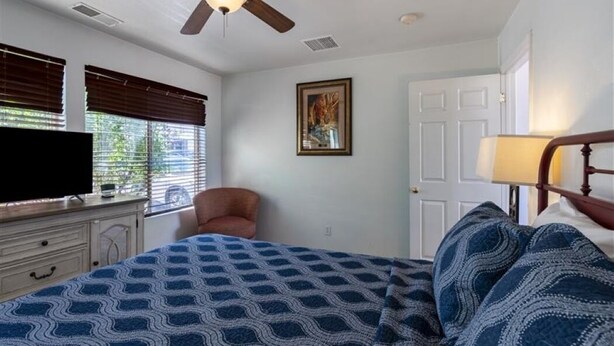 A bedroom with a bed, a ceiling fan, a dresser, a chair, a TV, a door, and a window with blinds. - Clean, Modern & Close to Everything Double Room At Silversage Inn (Moab)