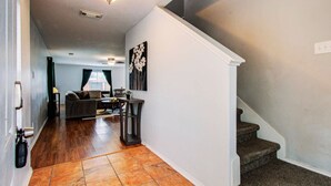 A hallway with a staircase, a living room with a sofa and a coffee table, and a painting on the wall. - Empress Modern Haven (Houston)