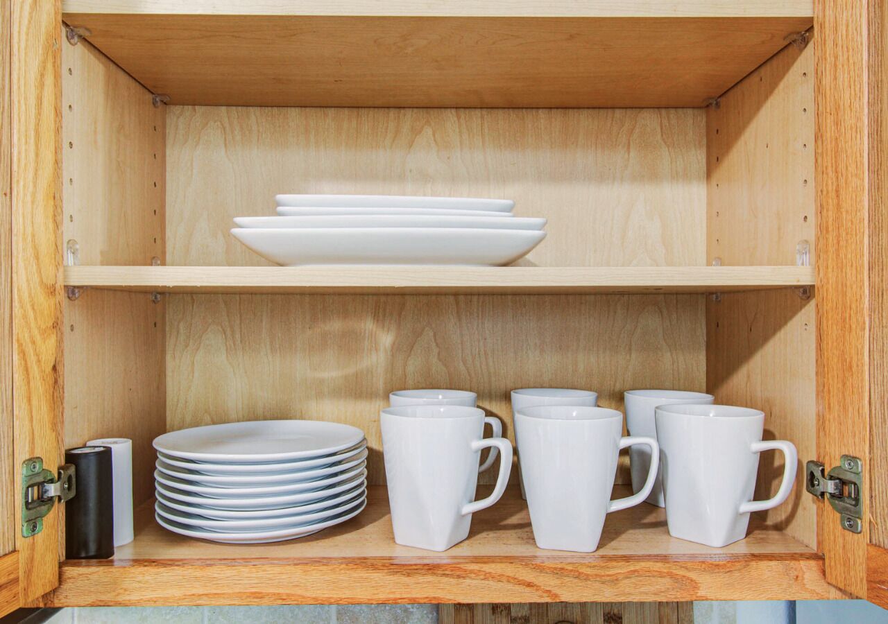 A wooden cabinet with shelves containing white plates and mugs.