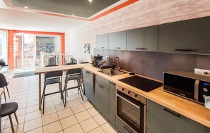 Cocina moderna con horno empotrado, microondas y un lavamanos. Hay dos sillas negras y una mesa de comedor.