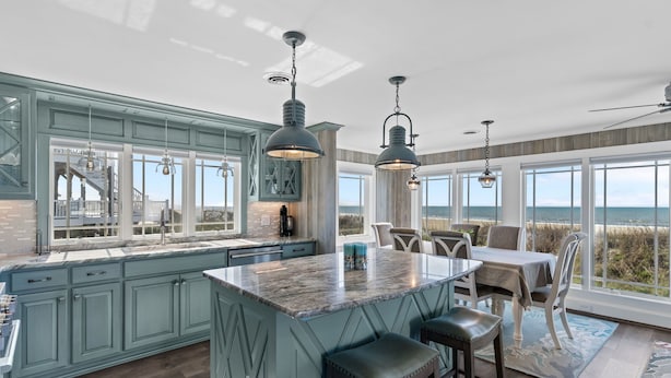 A kitchen with a large island, bar stools, and a dining table with chairs. - Reelaxing: Oceanfront Home in Yaupon Beach, Oak Island, Perfect for 9 guests! (Oak Island)