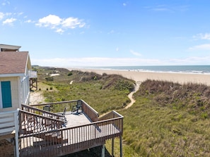 A beach house with a deck, a path leading to the beach, and a view of the ocean.