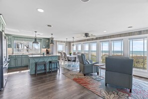 Una cocina amplia con una isla grande, comedor con sillas y vista a la playa.