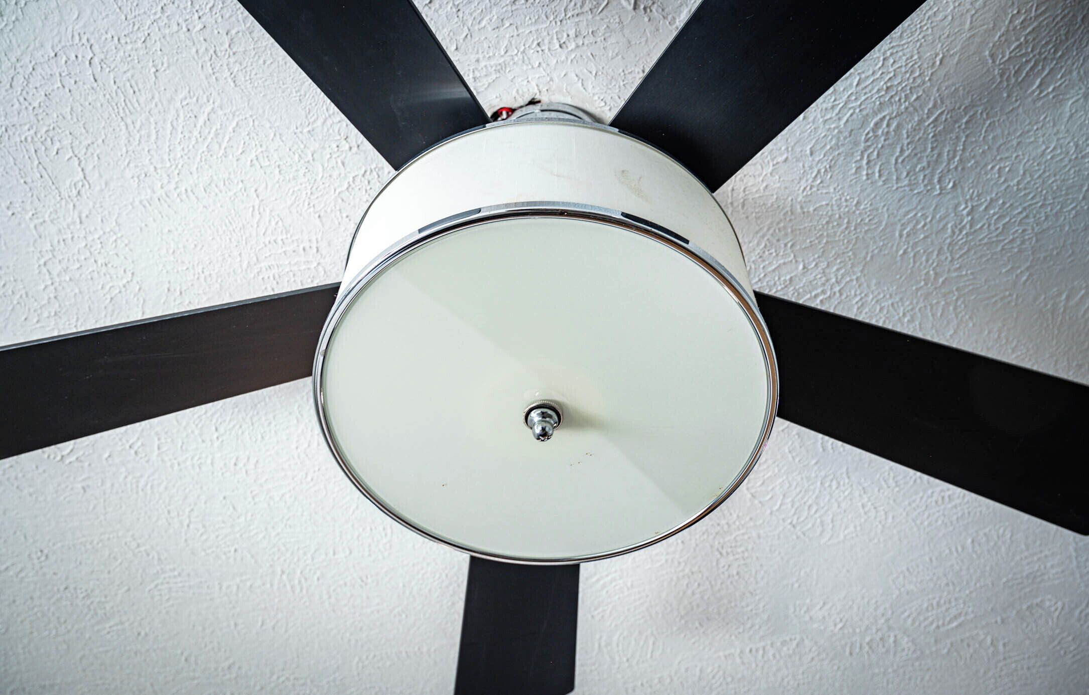 A ceiling fan with a white light fixture and four black blades.