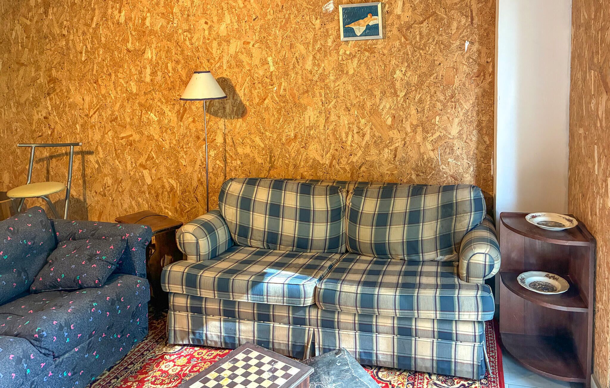 Un salon avec un canapé à carreaux, un fauteuil à motifs, une lampe et une petite table sur laquelle se trouve une assiette.
