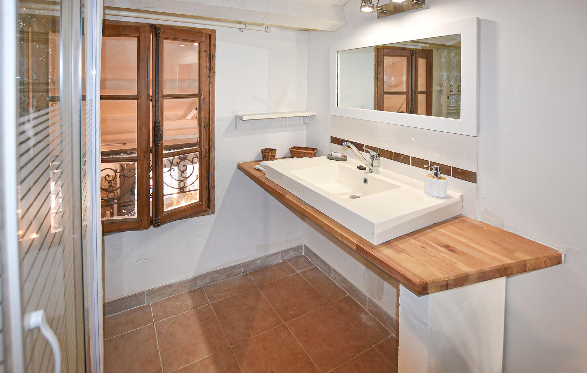 A bathroom with a large sink, wooden countertop, and a mirror above it.