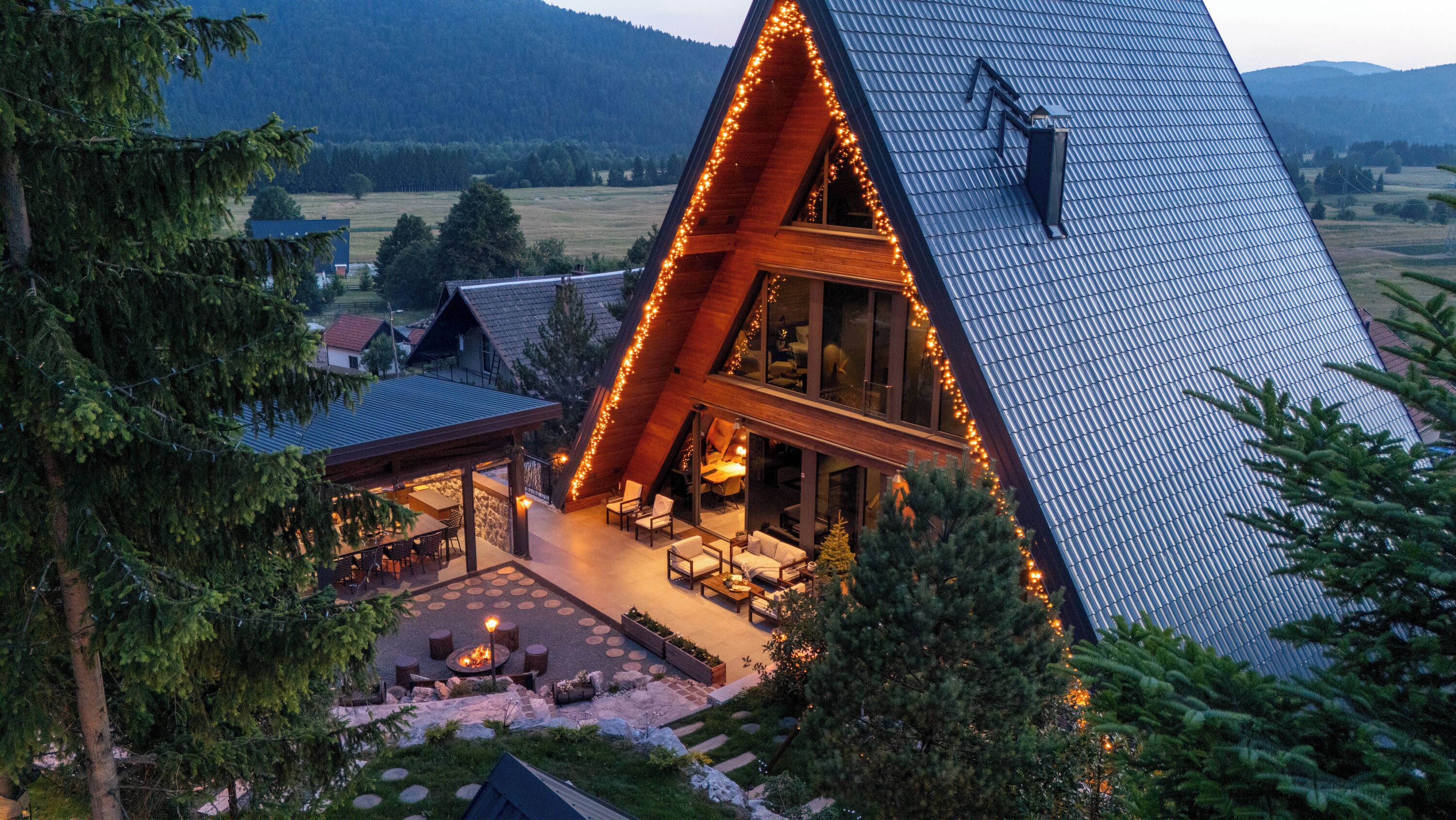Une maison moderne avec un toit en pente, de grandes fenêtres et un patio doté d’un espace salon extérieur.