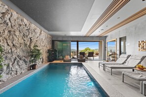 Ein Hallenbad mit Steinwand, Liegestühlen und Blick ins Freie.