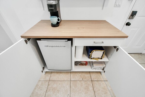Une petite cuisine équipée d’une machine à café, d’un petit réfrigérateur et d’un plan de travail en bois.