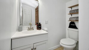 A bathroom with a white sink, mirror, and toilet. There are shelves above the toilet with towels and a black cap labeled 'hardyrier'. - Empress Sunlit Villa (Cypress)