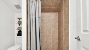 A bathroom with a toilet, a shower with beige tiles, and a white door.