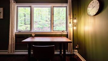 A room with a window, a clock, and a table with a chair.