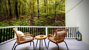 A wooden deck with wicker chairs and a small table, overlooking a forested area.