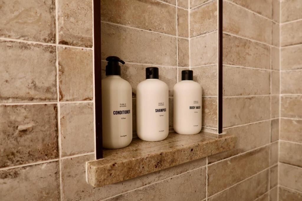 A bathroom shelf with three toiletry bottles labeled conditioner, shampoo, and body wash.