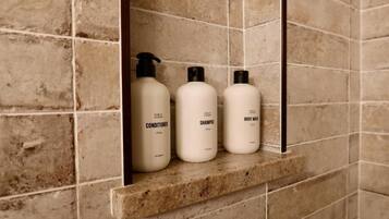 A bathroom shelf with three toiletry bottles labeled conditioner, shampoo, and body wash.