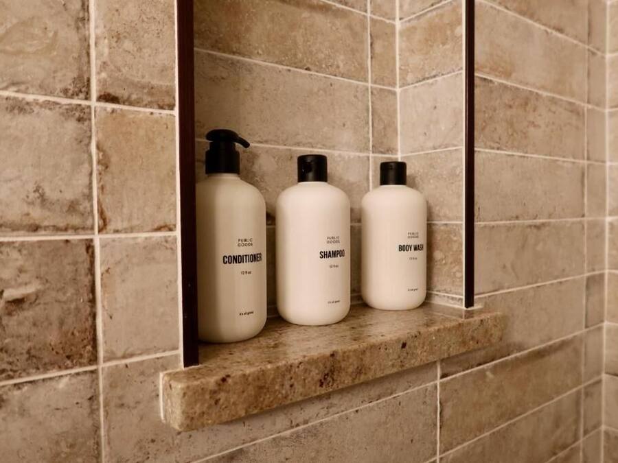 A bathroom shelf with three toiletry bottles labeled conditioner, shampoo, and body wash.