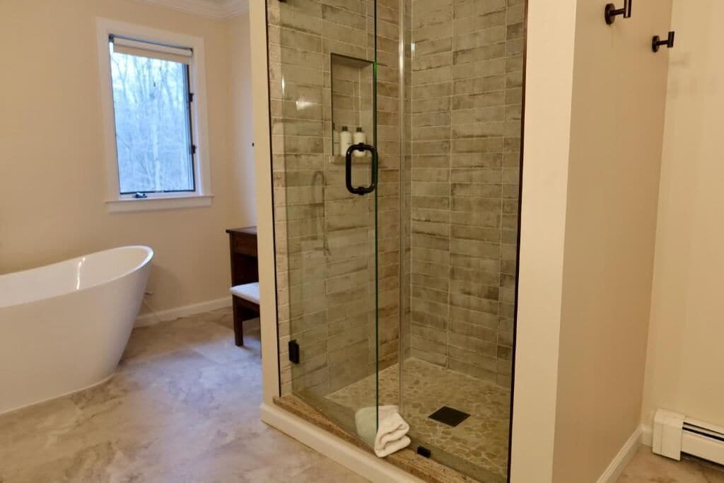Un baño con ducha de vidrio, bañera independiente y ventana.