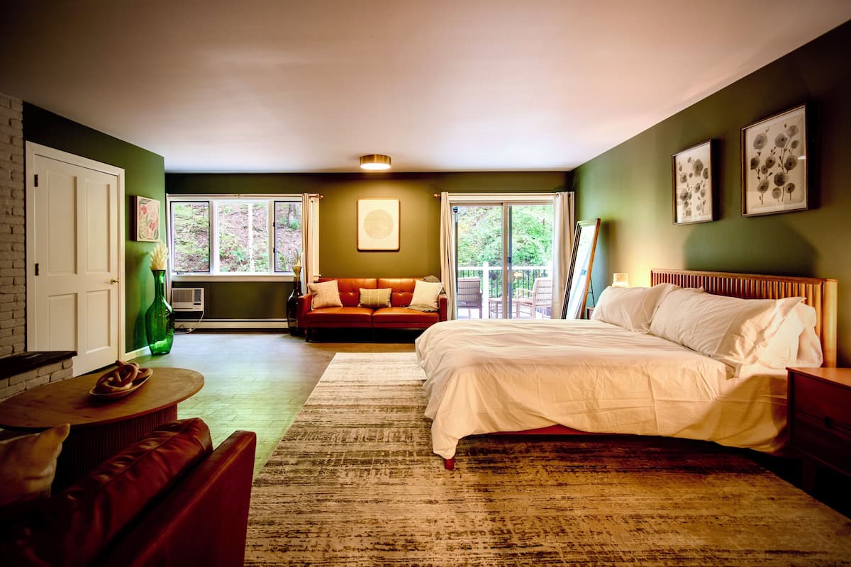 A bedroom with a bed, a sofa, a coffee table, and a window with curtains.