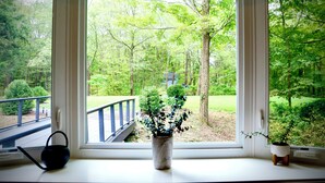 A window with a view of a forested area, a small potted plant, and a black kettle on the windowsill.